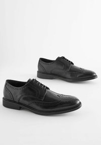 Chaussures habillées en cuir noir avec des détails perforés, bout pointu et design à lacets, présentant un petit talon et une texture lisse.