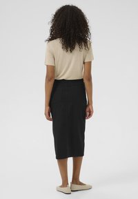 Jupe crayon en denim noir avec poches arrière, associée à un haut beige à manches courtes. Texture lisse, design mi-long et style minimaliste.