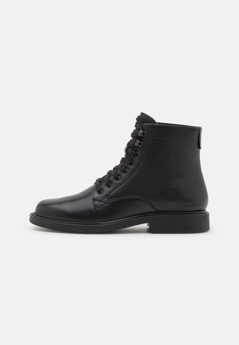 Černá kožená kotníková bota s rounded toe, šněrováním vpředu a nízkým plochým podpatkem. Má zadní poutko a prošívané detaily.