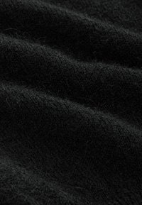 Tissu en tricot noir avec une texture douce, montrant de fins motifs et des plis délicats. Le matériau semble confortable et légèrement duveteux avec des fibres visibles.