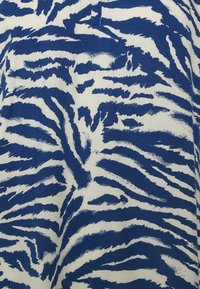 Baumwollstoff mit einem blau-weißen Tigerstreifenmuster, das eine strukturierte Erscheinung aufweist und einen kleinen Schlitz am Halsausschnitt hat.