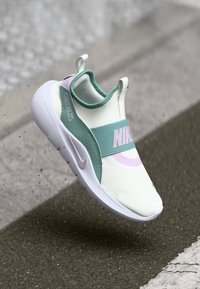 Nike tenisice s bijelim mrežastim gornjim dijelom, zelenim i ružičastim detaljima, elastičnom trakom i debelim bijelim potplatima, osmišljene za udobnost i podršku.