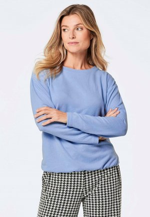 Hellblaues Fleece-Sweatshirt mit langen Ärmeln und Rundhalsausschnitt, kombiniert mit schwarzem und weißem Hahnentrittmuster-Hosen. Weicher Stoff.