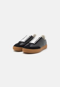 Sneakers with a black suede and patent leather upper, white laces, and a beige rubber sole, featuring white stitching and a smooth texture.