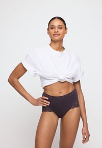 Witte cropped t-shirt met een knoopdetail aan de voorkant, gecombineerd met hoog uitgesneden donkerpaarse onderbroek met kanten rand.