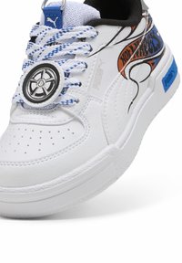 Zapatilla sintética blanca con acentos azules y negros, detalles con patrón, suela texturizada y un exclusivo mecanismo de bloqueo de cordones redondeado.