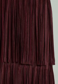 Burgundowa tkanina z frędzlami, wyposażona w pionowe paski o gładkiej fakturze, warstwowa konstrukcja nadająca płynny wygląd.