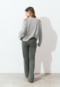 Striped long-sleeve top with cut-out shoulders in gray and white, paired with olive green flared pants featuring detailed back pockets.