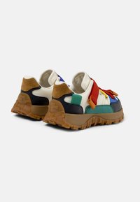 Mehrfarbige Sneaker mit einer Mischung aus Materialien wie Wildleder und Canvas, einer klobigen Gummisohle und kontrastierenden Schnürsenkeln in Rot und Blau.