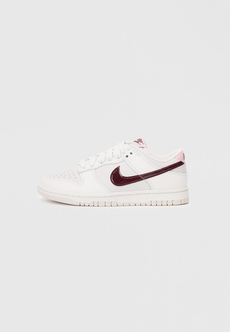 Witte sneaker met een gestructureerd oppervlak, verfraaid met een bordeauxrood lakleren swoosh. Beschikt over een lichtroze hieltab en witte veters.