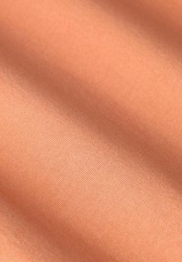 Perzikkleurige stof met een gladde, licht gestructureerde oppervlakte, die fijne ribbels en een zachte glans vertoont.