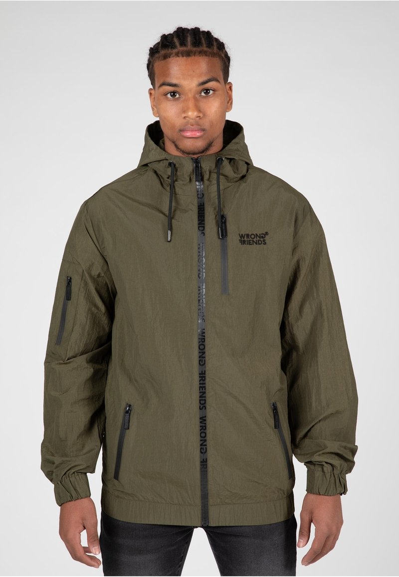 Olivegrüne leichte Jacke mit Kapuze, Reißverschluss vorne und Seitentaschen. Mit Logo-Druck entlang des Reißverschlusses vorne und elastischen Bündchen.
