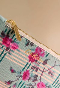 Maisiņš ar ziedu rakstu un mīļzaļas krāsas fonu. Aprīkots ar rāvējslēdzēju ar zelta detaļām un "Cath Kidston" zelta logotipu.