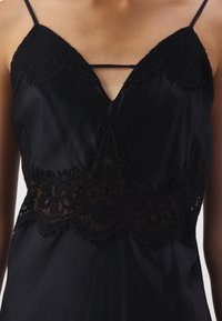 Camisole noire en soie avec bordure en dentelle le long du buste et de la taille, avec fines bretelles et une petite lanière horizontale au niveau de l'encolure.