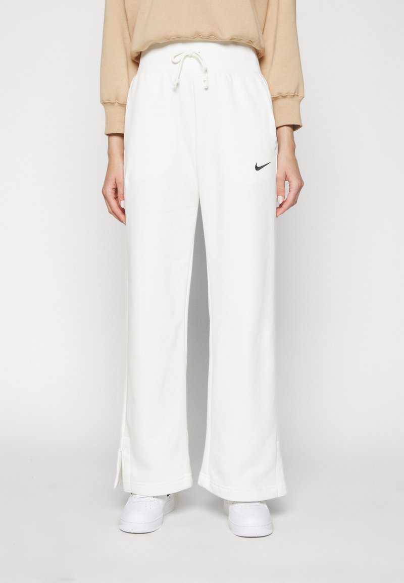 Weiße Jogginghose mit Kordelzugbund, weitem Bein, seitlichen Schlitzen am Saum und einem kleinen schwarzen Nike-Logo auf der linken Vorderseite.
