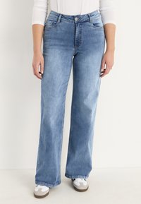 Ljusblå vida jeans i denim, med fem fickor, dragkedja med metallknapp och en subtil tvättad textur.