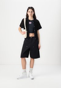 Black open-knit short-sleeved cardigan, black cropped top, black shorts, white sneakers, beige shoulder bag, textured fabric, and casual fit.