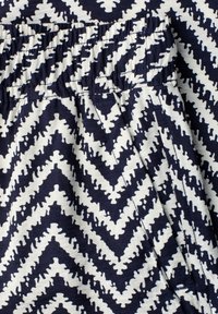 Gros plan d’un tissu à motif zigzag bleu marine et blanc avec une ceinture élastique et des coutures de poche sur la couture latérale.
