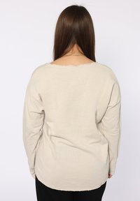 Maglietta beige a maniche lunghe con scollatura ampia e orli sfilacciati. Realizzata in un tessuto morbido, presenta una vestibilità comoda e un orlo arrotondato.