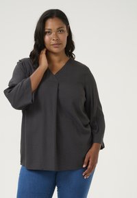Blouse gris foncé avec un décolleté en V et des manches trois-quarts. Présente un motif texturé et une coupe décontractée, associée à un jean bleu.