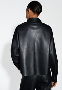 Giubbotto in pelle nera con una vestibilità comoda, caratterizzato da un colletto classico, una texture liscia e cuciture visibili lungo la cucitura posteriore.