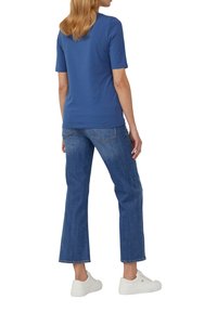 Chemise bleue à manches courtes avec une coupe ajustée, associée à un jean évasé bleu clair et des baskets blanches, vue de dos.
