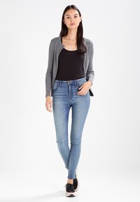 Cardigan gri cu dungi, purtat peste un top negru, asociat cu blugi slim-fit de culoare albastru deschis și adidași negri cu accente roz.