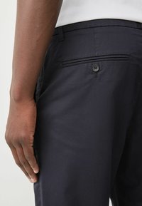 Chinos navy en tissu lisse, dotés d'une poche latérale et d'une poche arrière à boutons. Leur design ajusté présente une coupe régulière.