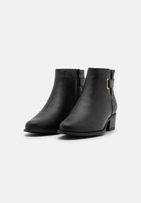 Bottines noires en cuir lisse, dotées d'une fermeture éclair sur le côté, d'un panneau matelassé et d'un petit talon bloc pour plus de stabilité.