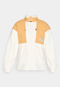 Zipepová fleece bunda v bielej a svetlo žltej farbe s vysokým golierom, dvoma náprsníkovými vreckami a kontrastným prešívaním. Hladká textúra.