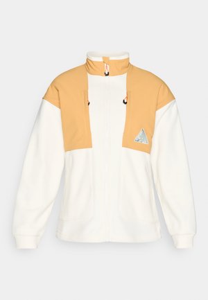 Φλις μπουφάν με φερμουάρ σε λευκό και ανοιχτό κίτρινο, με υψηλό γιακά, δύο τσέπες στο στήθος και λεπτομέρειες σε αντίθεση στο ράψιμο. Απαλή υφή.