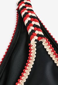 Juodas bikini viršus su pynimo apdaila raudona, smėline ir juoda spalvomis. Papuoštas tekstūruota pintine medžiaga ir mažais pom-pom akcentais palei kraštus.