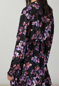 Svart blommig klänning i lätt tyg, med långa ärmar, cinchad midja och volangkant med flerfärgade blommönster.