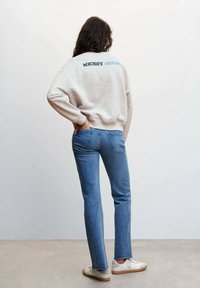Felpa grigia con il testo "MICKEY MOUSE" in blu sul retro, abbinata a jeans in denim azzurro chiaro e sneakers bianche.