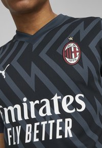 Černá a šedá sportovní dres s cik-cak vzorem, s límcem ve tvaru V, logem Puma a emblémem AC Milán s hvězdou nad ním.