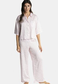 Ensemble de pyjama en satin rose clair comprenant un haut à manches courtes avec boutons et une poche sur la poitrine, ainsi que des pantalons amples assortis à un motif léopard discret.