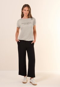 Camiseta corta de manga con un diseño impreso en color gris claro, combinada con pantalones holgados negros y zapatillas blancas. Textura suave, ajuste casual.