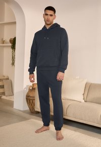 Mörkblå hoodie och matchande joggingbyxor i mjukt, strukturerat tyg, med framficka och elastiska muddar. Minimalistisk design.