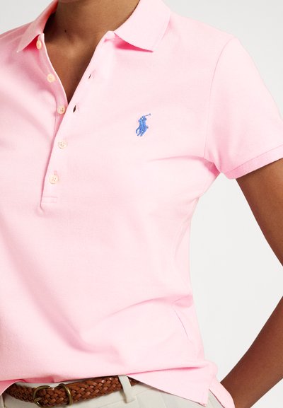 Šviesiai rožinė polo marškinėliai iš medvilnės, turintys klasikinį apykaklę, tris mygtukus ir mėlyną išsiuvinėtą logotipą ant krūtinės.