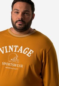 Senfgelbe Langarm-Sweatshirt mit weißem "VINTAGE"-Text, Fußballgrafik und zweifarbigem Kragen-Detail. Baumwollmischgewebe.