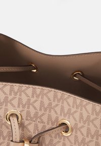 Sac à main beige Michael Kors avec motif monogramme MK, œillets dorés et fermeture à cordon en cuir beige partiellement ouverte, montrant la doublure intérieure lisse.