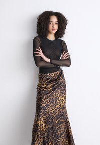Top negro transparente de mangas largas con un diseño ajustado, combinado con una falda de satén de estampado de leopardo con tejido drapeado y una forma fluida.