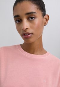 Różowy bawełniany t-shirt z okrągłym dekoltem, z małym haftowanym logo na piersi. Gładka faktura i luźny krój.