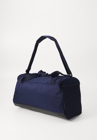 Sac de sport bleu marine avec une fermeture éclair sur le dessus, deux poignées de sangle et une base noire texturée. Présente des détails en maille sur un côté.