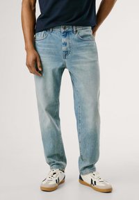 Hellblaue Jeans aus Denim mit lockerer Passform, Fünf-Taschen-Design und sichtbaren Nähten. Kombiniert mit weißen und schwarzen Sneakers.