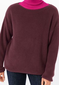 Suéter de punto acanalado de gran tamaño en burdeos oscuro con hombros caídos. Capa sobre un cuello tortuga rosa brillante, creando un atrevido contraste de colores.