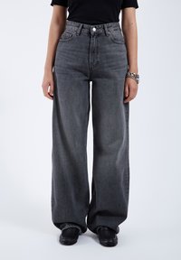 Weit geschnittene graue Denim-Jeans mit hoher Taille, einem einzelnen vorderen Knopf und standardmäßiger fünf Taschen-Design, mit einer leicht ausgewaschenen Textur.
