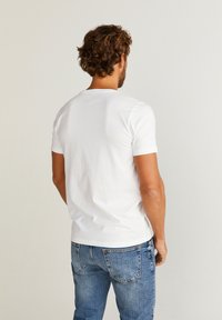 Hvid t-shirt med korte ærmer og rund halsudskæring, lavet af bomuld, båret med blå denimjeans, der viser en afslappet pasform bagfra.