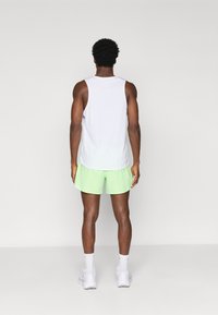 Λευκή αμάνικη αθλητική μπλούζα και ανοιχτό πράσινο σορτς. Το μοντέλο στέκεται με πλάτη, με λευκά αθλητικά παπούτσια και χαμηλές λευκές κάλτσες. Απλός σχεδιασμός.