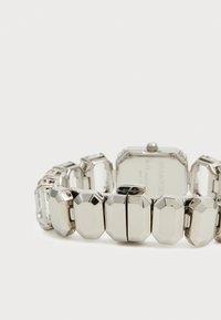 Silver-tone watch with a geometric metal bracelet, featuring rectangular and octagonal links, and a square watch face on the back.